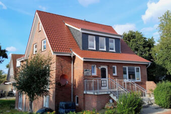Two-story red brick house with red tiled roof and front stairs surrounded by trees and shrubs at Fewos Haus am W&auml;ldchen