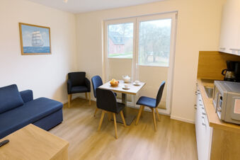 Living area at Fewos Haus am W&auml;ldchen with blue sofa, small dining table with four chairs, coffee machine and microwave visible