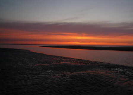 sunset over a calm water body and wet beach area captured near Fewos Haus am W&auml;ldchen with orange and purple sky tones