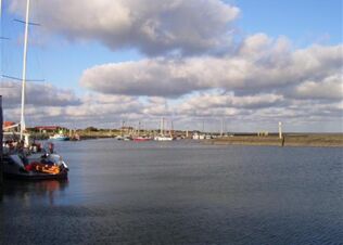 Sailboats and small boats docked in a calm harbor under cloudy skies near Fewos Haus am W&auml;ldchen's coastal area