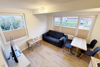 Living room at Fewos Haus am W&auml;ldchen with a black sofa, wooden coffee table, dining table with chairs, and TV near windows