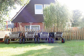 Four black and one beige Feldmann&rsquo;s Bollerwagen carts with contact numbers are lined up in front of a house at Fewos Haus am W&auml;ldchen