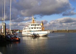 A large white ferry boat approaches a dock with cranes and smaller boats in harbor near Fewos Haus am W&auml;ldchen