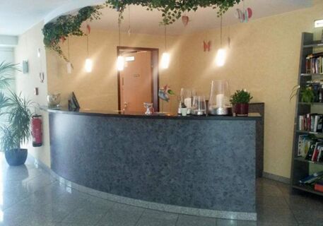 Curved gray reception desk with decorative candles and plants under hanging lights in the Apartments Aschheim lobby area