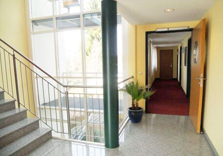 Staircase with metal railing and granite steps next to hallway with potted plant in Apartments Aschheim interior design
