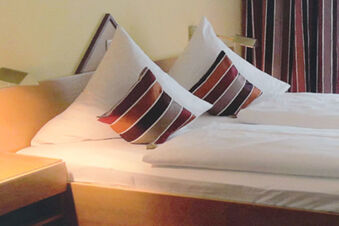 Hotel-Caf&eacute; 3 Kronen'de iki yataklı, &ccedil;izgili yastıklı ve sıcak aydınlatma konseptli rahat otel odası.