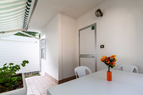White patio with plastic chairs and table with orange flowers in a vase outside room 117 at Marina Romea Easy Camping Village