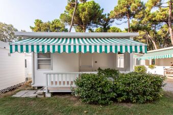 Small white bungalow with a green and white striped awning and green bushes in front at Marina Romea Easy Camping Village
