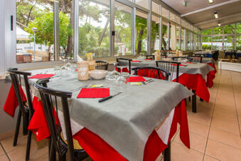 Dining area with tables covered in red and gray tablecloths set with glasses and cutlery at Marina Romea Easy Camping Village