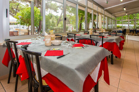 Dining area with tables covered in red and gray tablecloths set with glasses and cutlery at Marina Romea Easy Camping Village