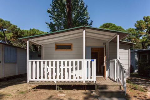 White wooden cabin with covered porch and outdoor chairs surrounded by trees at Marina Romea Easy Camping Village