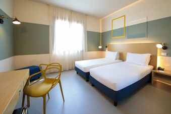 Two twin beds with white linens under modern wall lamps and window covered by sheer curtains in B&B Hotel Mantova Cristallo room