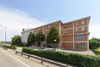 B&B Hotel Mantova Cristallo building with brick facade, multiple windows, trimmed trees, parked cars, and a clear blue sky above