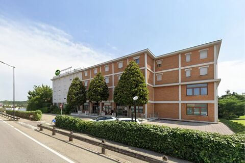 B&B Hotel Mantova Cristallo building with brick facade, multiple windows, trimmed trees, parked cars, and a clear blue sky above