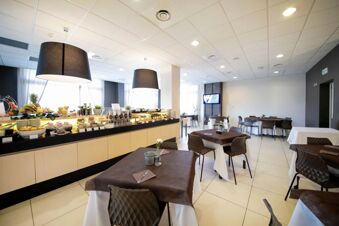Dining area of B&B Hotel Mantova Cristallo with tables covered in brown and white cloths, chairs, and buffet counter with food and fruit
