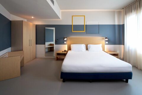 Double bed with white linens between two nightstands in a hotel room with wooden wardrobe and mirror at B&B Hotel Mantova Cristallo