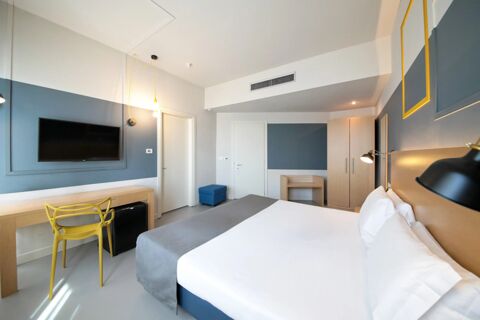 Modern hotel room at B&B Hotel Mantova Cristallo with a large bed, yellow chair, wall-mounted TV, and wooden furniture