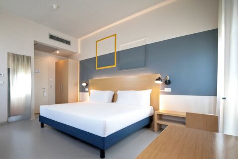 Double bed with white bedding and pillows in a minimalist room at B&B Hotel Mantova Cristallo with blue and white walls and wooden furniture