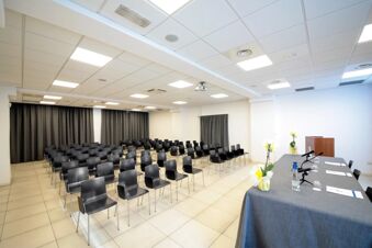 Conference room at B&B Hotel Mantova Cristallo with rows of black chairs, a table with microphones, and tiled flooring