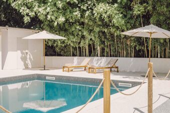 Swimming pool area with wooden lounge chairs, white umbrellas, and green trees in the background at B&B Hotel Mantova Cristallo