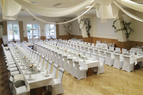 A banquet hall at Land-gut-Hotel Seeblick with long tables set for dining, white chairs, floral decorations, and draped ceiling fabric