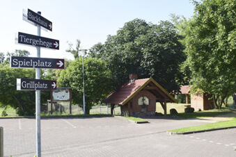 Signpost with four directional signs in German next to a small brick oven shelter among trees at Land-gut-Hotel Seeblick