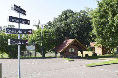 Signpost with four directional signs in German next to a small brick oven shelter among trees at Land-gut-Hotel Seeblick