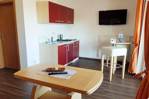 Room interior at Land-gut-Hotel Seeblick with small kitchenette, wall-mounted TV, wooden table, and tall chair by window