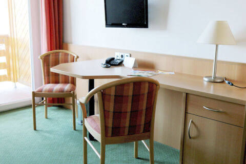 Two wooden chairs with orange striped upholstery, a desk with a lamp, a telephone, and a wall-mounted TV in Land-gut-Hotel Seeblick room