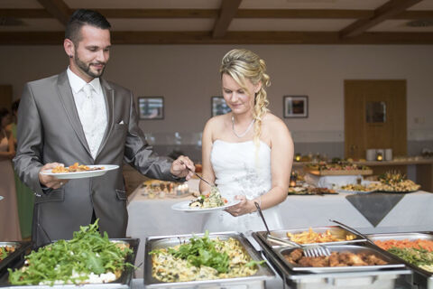 Bride and groom serving themselves food from buffet trays at a wedding reception in Land-gut-Hotel Seeblick banquet hall