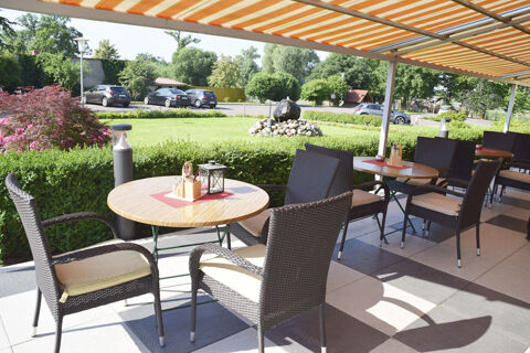 Outdoor seating area with round tables and cushioned wicker chairs under an orange-striped awning at Land-gut-Hotel Seeblick