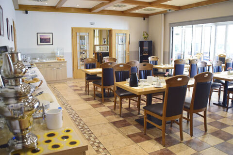 Dining area with wooden tables and chairs set for breakfast near a buffet table in Land-gut-Hotel Seeblick