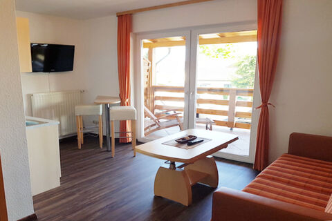 Living area with a striped sofa, wooden coffee table, small dining table with two stools, and balcony in Land-gut-Hotel Seeblick