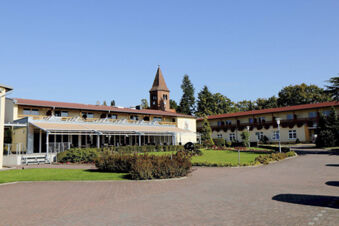 Land-gut-Hotel Seeblick building with red roof, covered terrace, green garden, brick driveway, and church tower in background