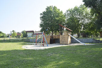 Playground with wooden play structure, slide, and swings on grass near trees at Land-gut-Hotel Seeblick