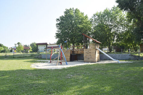Playground with wooden play structure, slide, and swings on grass near trees at Land-gut-Hotel Seeblick