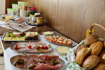 En varierad frukostbuff&eacute; med kallskuret, ost, lax och br&ouml;drullar i ett tr&auml;panelat h&ouml;rn p&aring; Gasthof Pension R&ouml;per-Bolte.