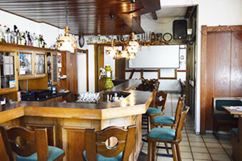 Traditionell hotellbar med tr&auml;b&auml;nk, pallar och dekorativa lampor i en mysig atmosf&auml;r i Gasthof Pension R&ouml;per-Bolte.