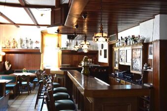 Interi&ouml;rvy av baren p&aring; Gasthof Pension R&ouml;per-Bolte med tr&auml;m&ouml;bler, bardisk och bekv&auml;ma sittplatser i varmt ljus.