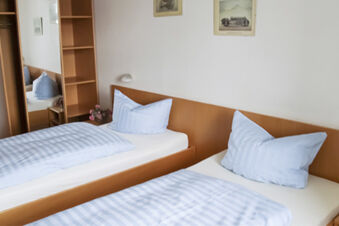 Enkelt inrett dubbelrum med ljusbl&aring; s&auml;ngkl&auml;der och tr&auml;m&ouml;bler p&aring; Gasthof Pension R&ouml;per-Bolte.