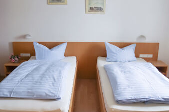 Enkelt inrett dubbelrum med tv&aring; enkels&auml;ngar, bl&aring; t&auml;cken och kuddar p&aring; Gasthof Pension R&ouml;per-Bolte.