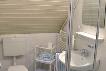 Litet badrum med toalett, handfat och handdukar i Gasthof Pension R&ouml;per-Bolte under ett sluttande tak.