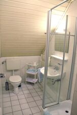 Ljust badrum med vitkaklade v&auml;ggar och golv i Gasthof Pension R&ouml;per-Bolte med dusch, handfat, toalett och handdukar.