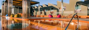 Outdoor swimming pool area at Nhow Milano with lounge chairs, colorful bean bags, and reflective glass panels