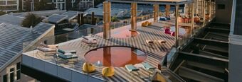 Outdoor terrace at Nhow Milano with circular pools, lounge chairs, yellow bean bags, and glass railings in daylight