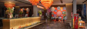 Reception area with a golden front desk, orange hanging lights, colorful wall art, and decor at Nhow Milano hotel