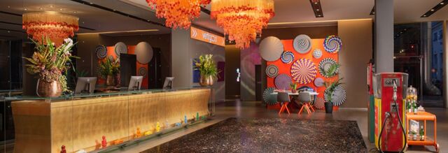 Reception area with a golden front desk, orange hanging lights, colorful wall art, and decor at Nhow Milano hotel