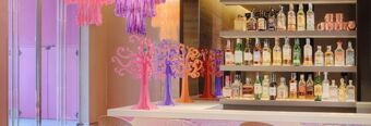 Rows of assorted liquor bottles on illuminated shelves behind a white counter with colorful decorative stands at Nhow Milano