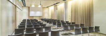 Conference room with rows of gray chairs facing a projector screen in a modern setting at Nhow Milano