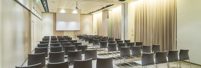 Conference room with rows of gray chairs facing a projector screen in a modern setting at Nhow Milano